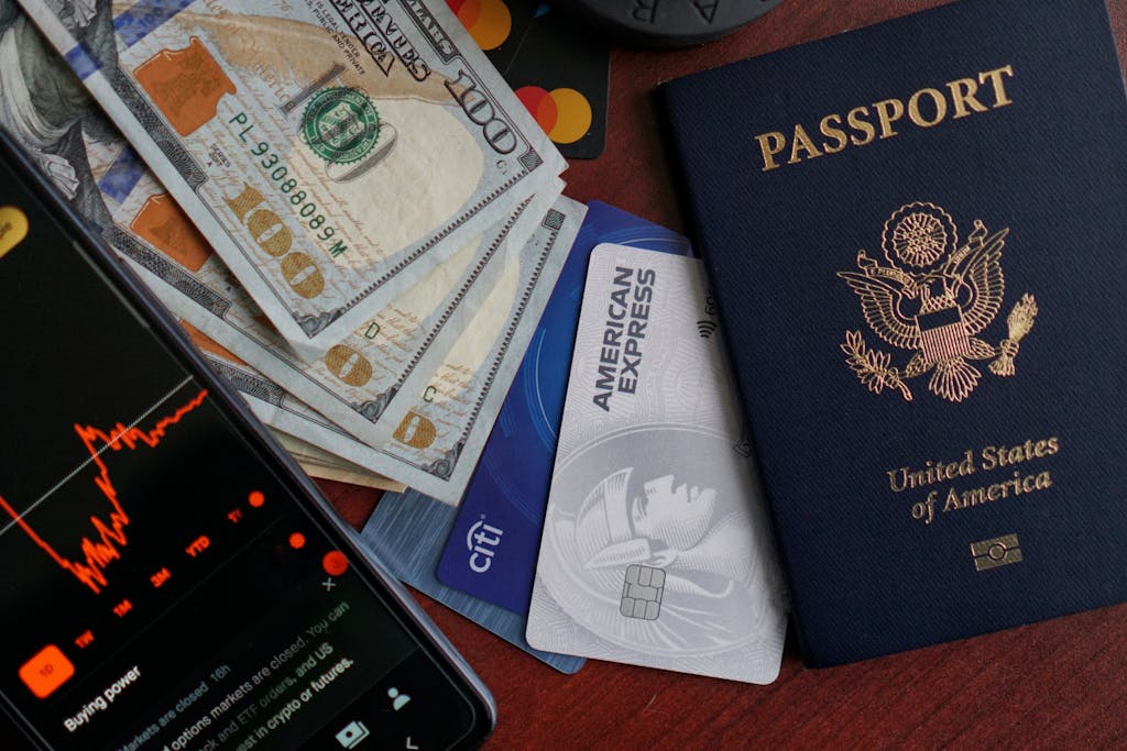 Top view of US passport, credit cards, cash, and phone showing financial graph, ideal for travel themes.